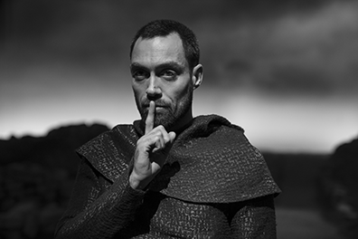 Macbeth-Ross 0108 Alex Hassell as the Thane of Ross, in chainmail shirt and cloaked shoulder with his finger up to his lips in a "silence" gesture (black and white photograph).