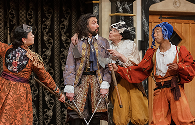 ASC-Two_Gentlemen_of_Verona-240 Valentine in light purple coat and colorful cavalier breeches has swords in both hands pointing down as he surrenders to the three outlaws in various ragged Jacobean clothes and masks pulled up on their foreheads.