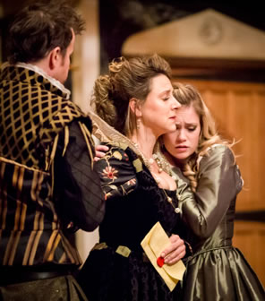 Isabella snuggles up to Livia's shoulders, their eyes closed, and Livia holding a red-sealed letter in her hand with Hippolito standing to her other side.