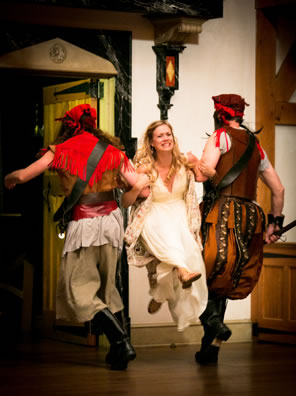 Mirana between two pirates, their backs to the audience, she facing the audience, off the ground her feet kicking as they carry her off. She's ina beautifully trimmed white dress with pastel floral cape, the pirates are, well, pirates.