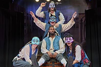 Faction of Fools Commedia Romeo & Juliet: Mab The 2024 Capulet cast in blue vests, all in masks except Romeo, form the Queen Mab visual: Mercutio on top speaking, then Benvolio with arms outstretched, Romeo listening, two servants at the bottom.