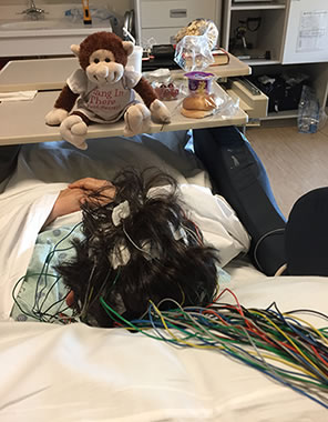 Photo of the back of Sarah in the hospital room, taken from the head with multiple colored wires stringing across the pillow.