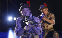 Scottish solders with the red plumes in their berets kneel with rifles poised and what looks like car headlights shining from the back